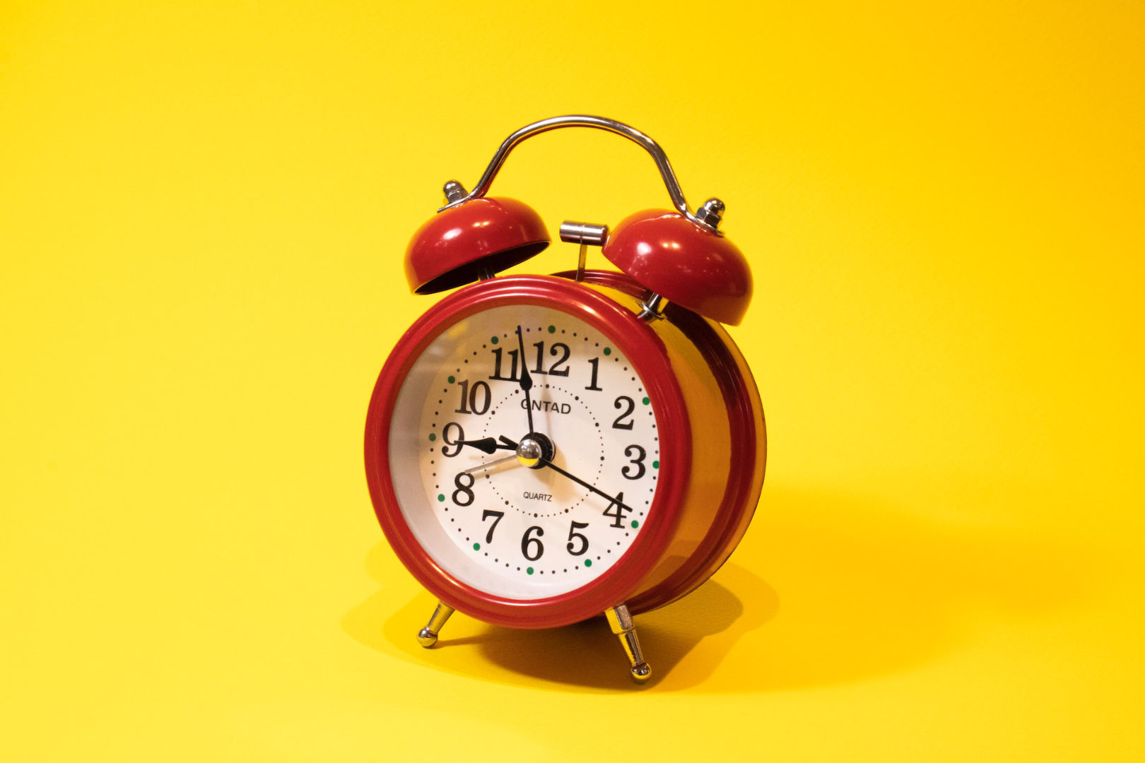 A red alarm clock in a bright yellow background.