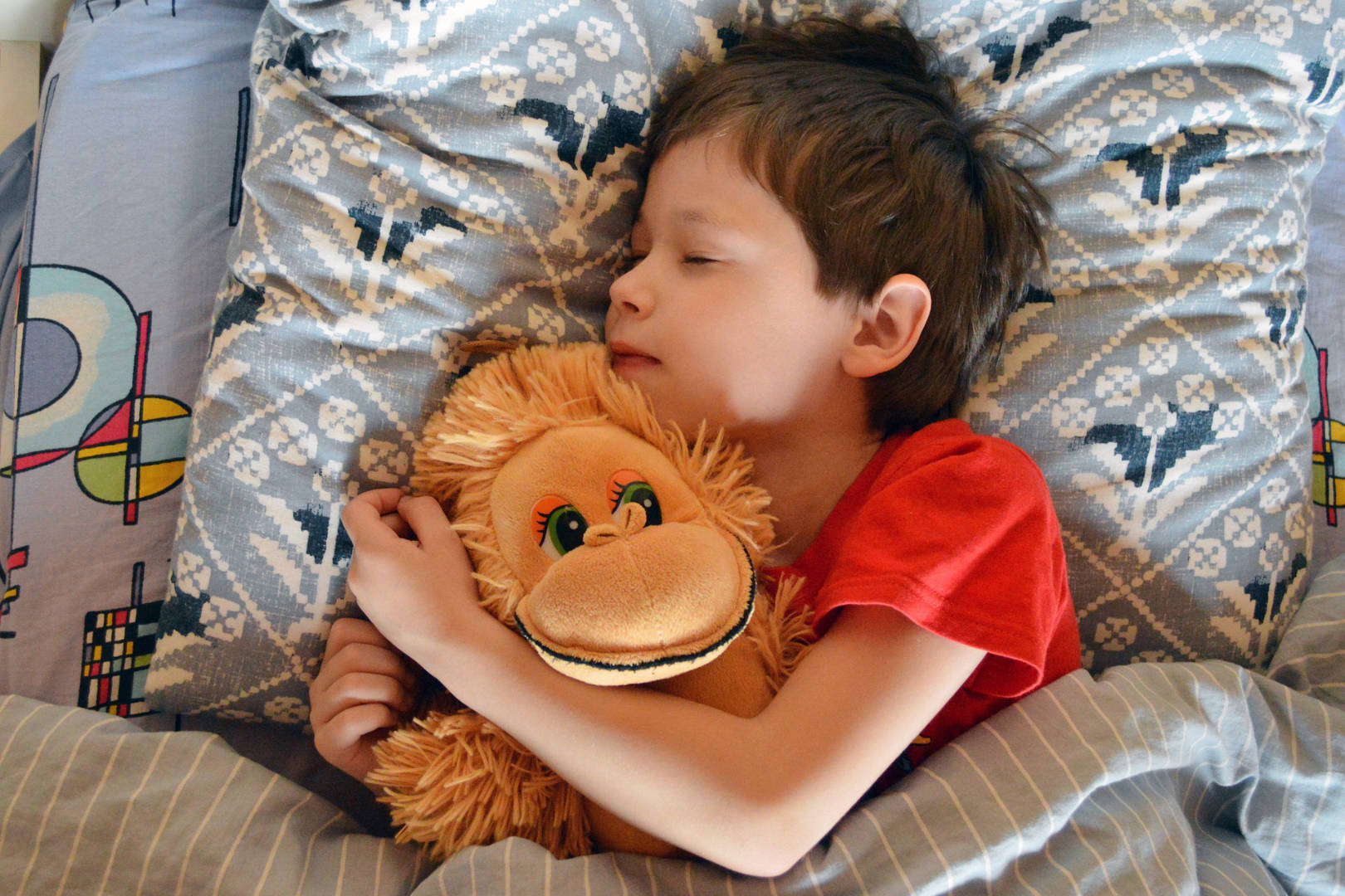 A boy sleeping while cuddling a plush toy.