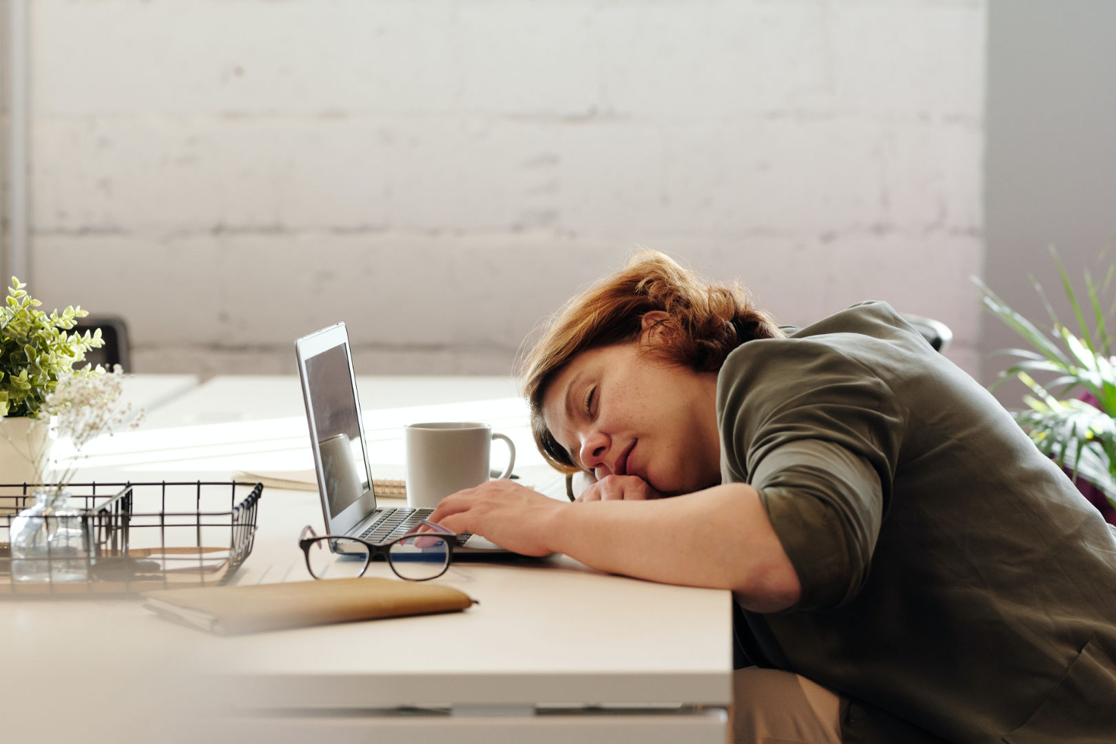 A woman accidentally falls asleep on the desk while working on her laptop.