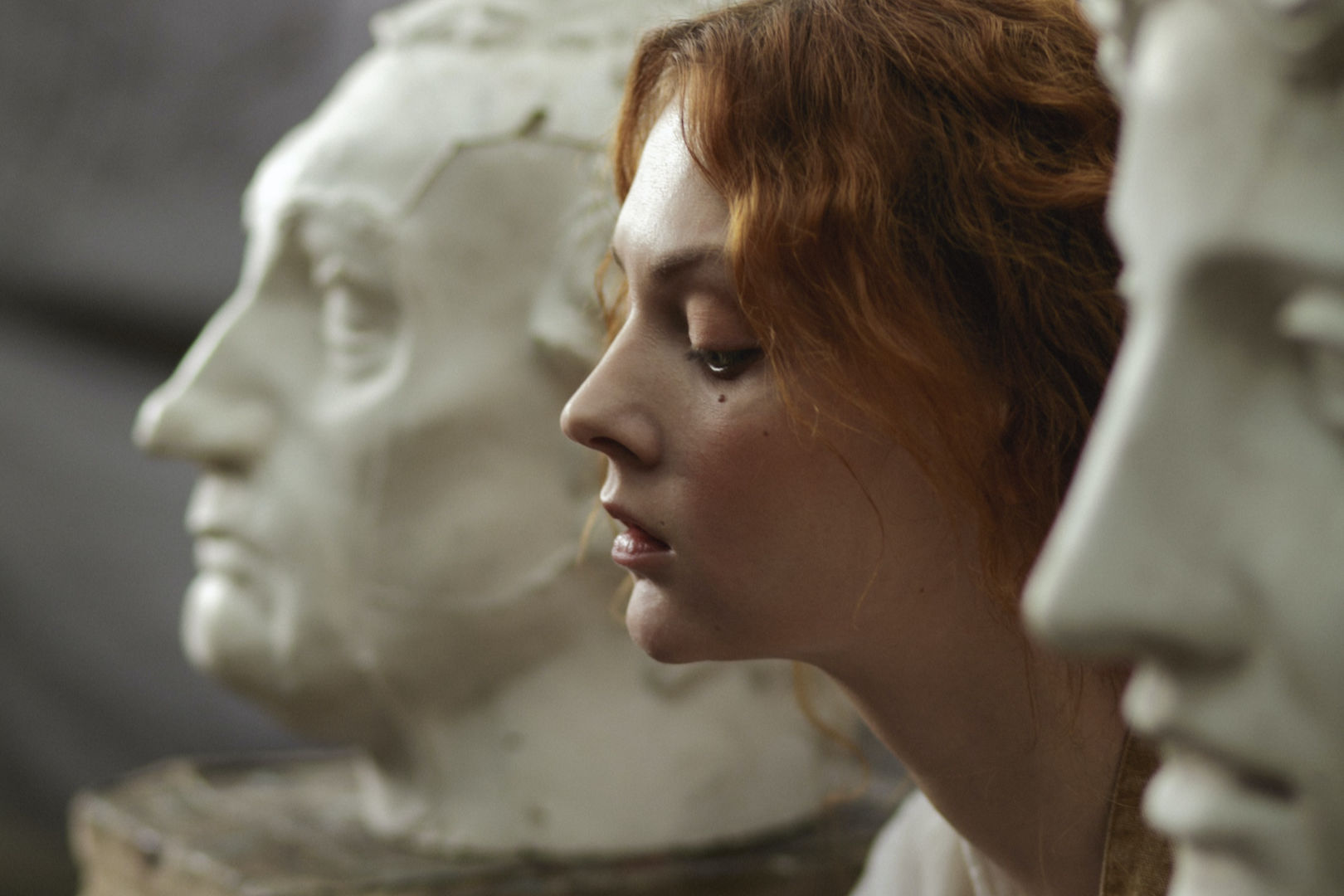 A close-up shot of a woman in between two faces of white statues.