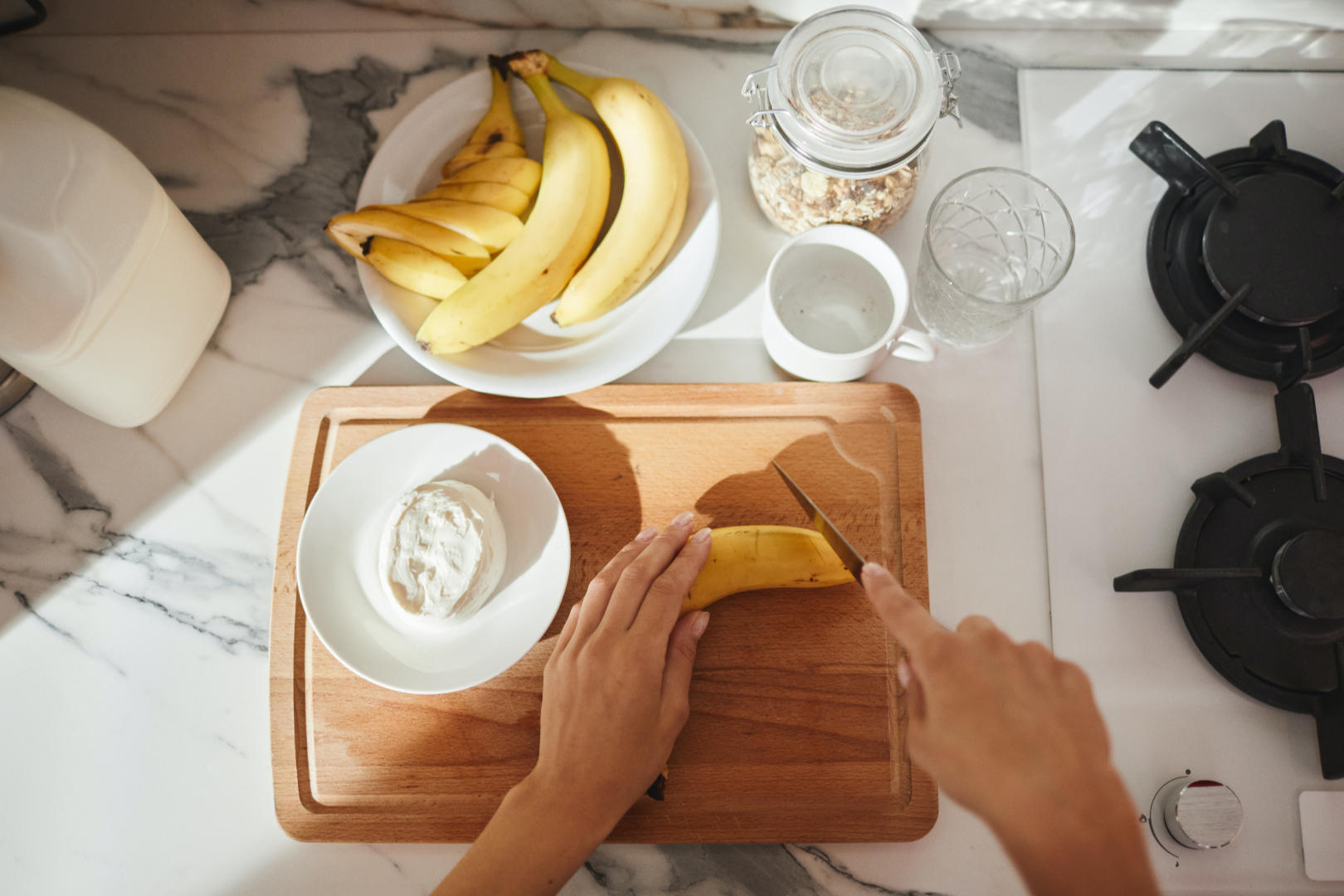 A person in a kitchen preparing a ripe banana on a wooden cutting board.