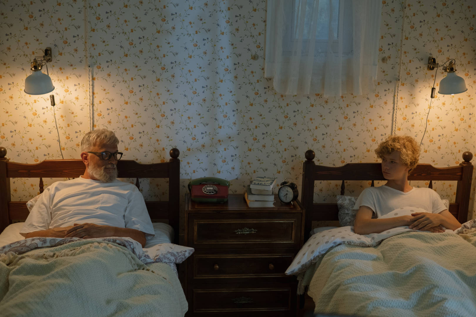A father and son lying on separate beds and looking at each other.