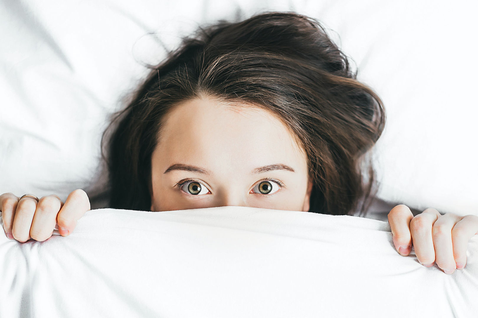 A woman looking directly while covering half of her face with a white blanket.