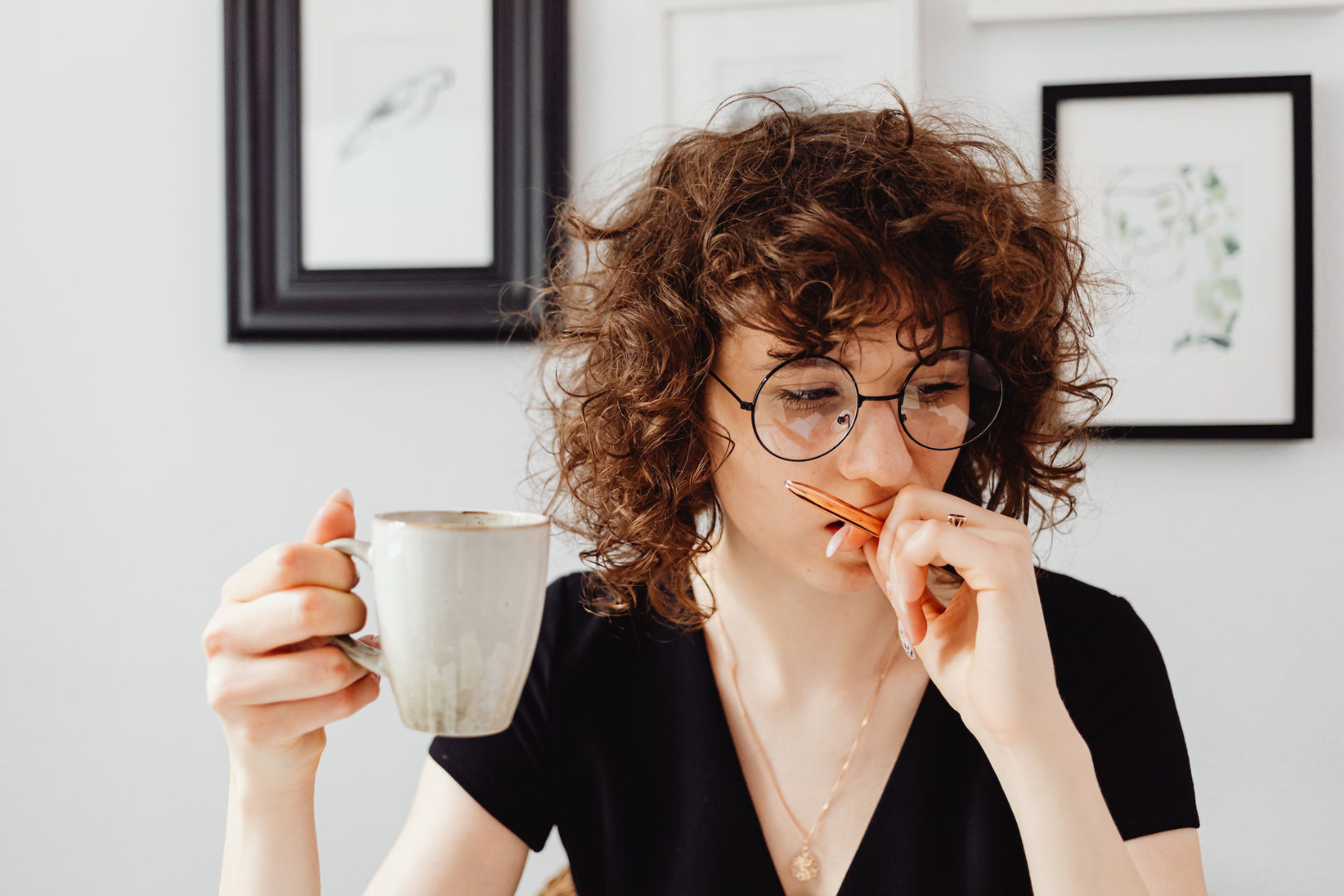 A short-haired woman holding a mug and a pen while looking serious and concerned.