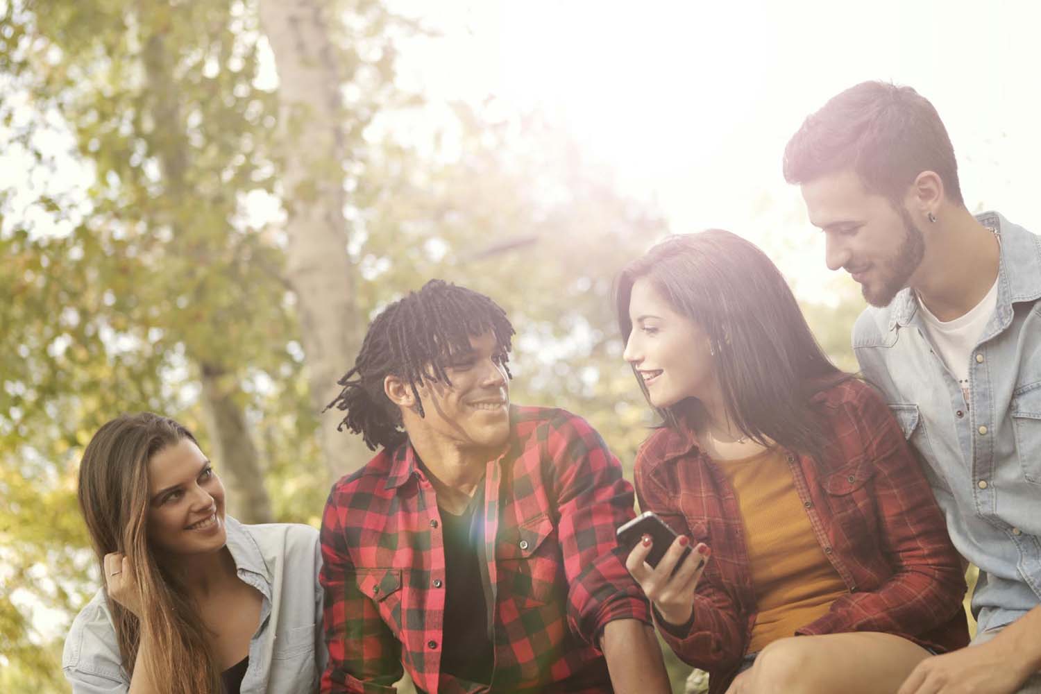 four friends sitting outside smiling and holding a cell phone