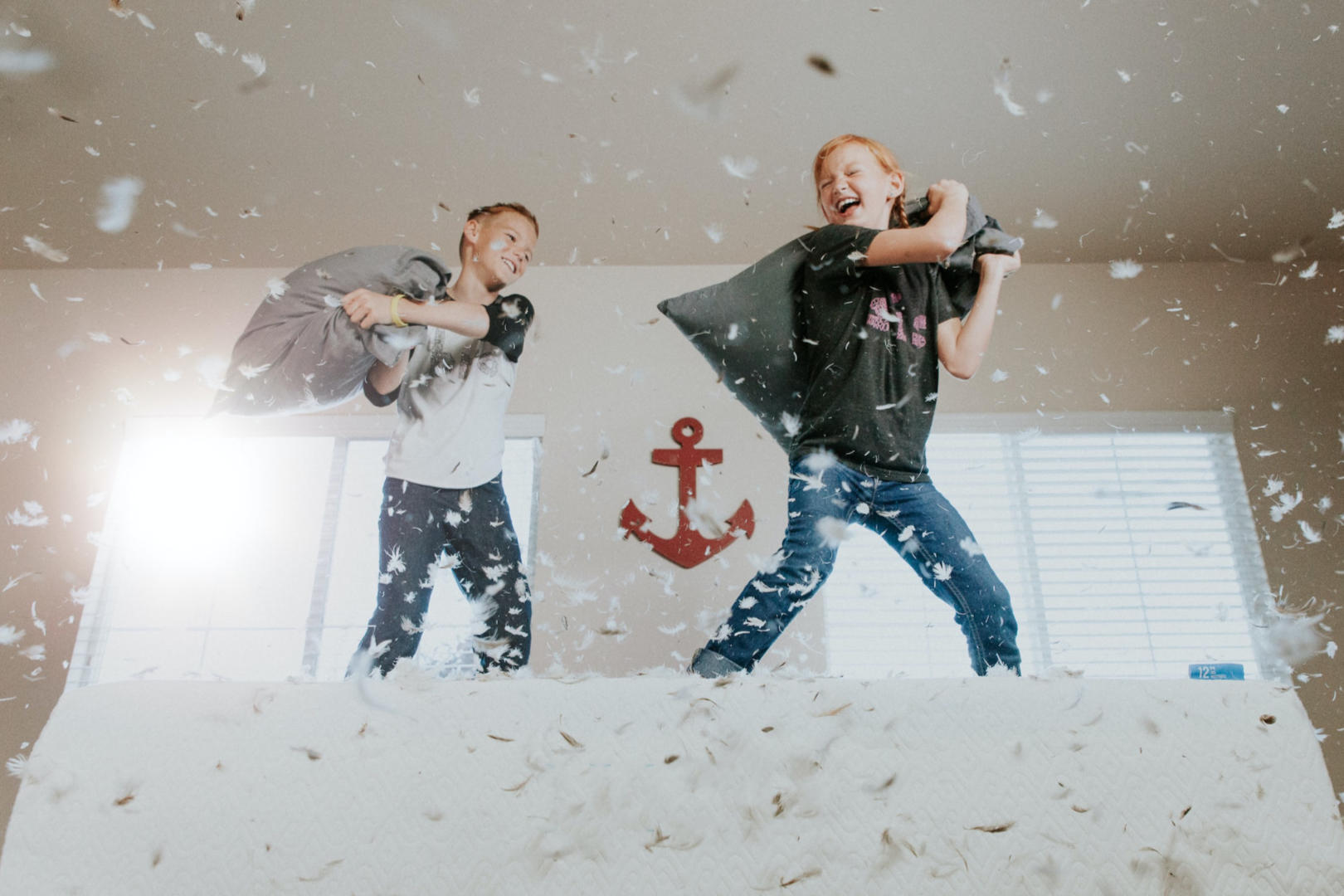 Two children having fun with a pillow fight on top of a bed.