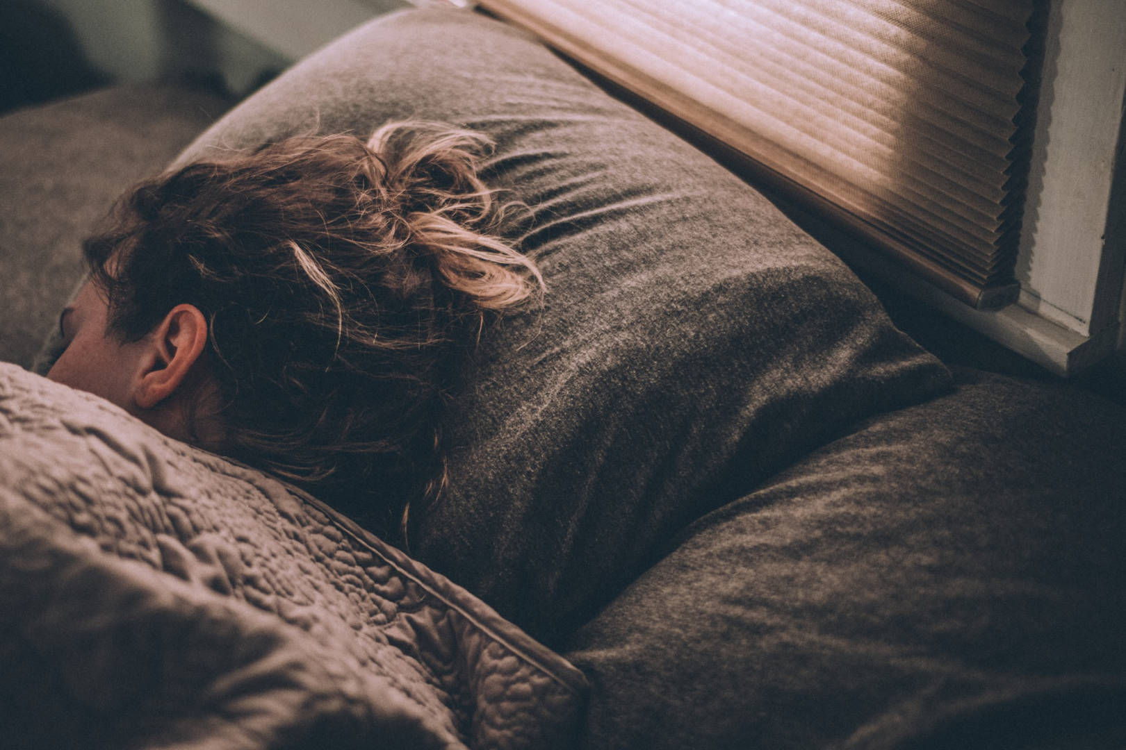 A woman sleeping on bed covered in blanket in a dark room.