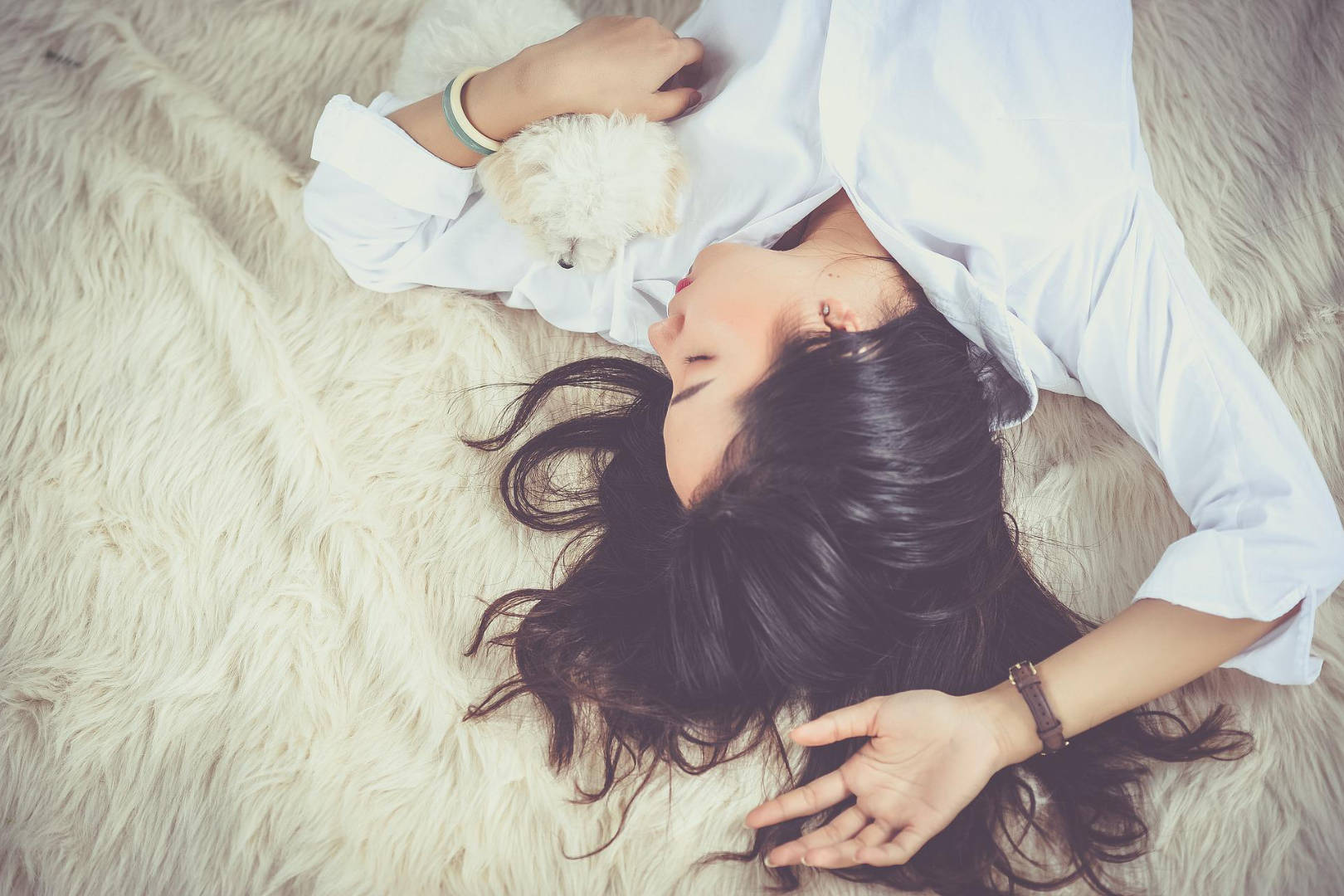 A woman in deep sleep while cuddling a white cute puppy.
